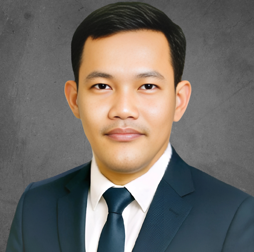 A person wearing a dark suit and tie, posing against a textured, gray background.