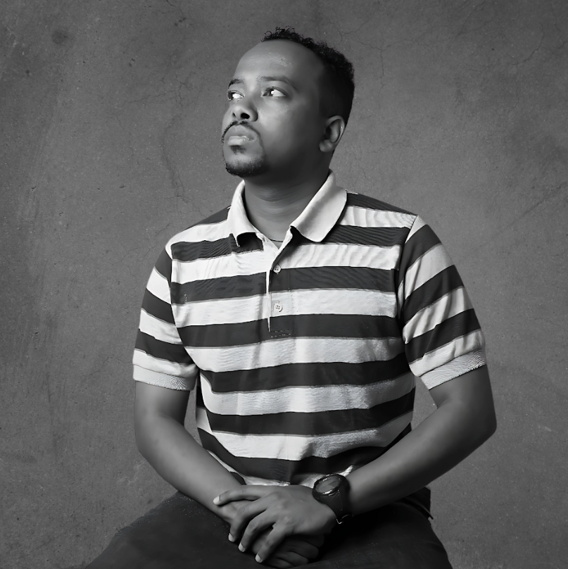 A person is seated, looking upward, wearing a striped polo shirt and a watch. The background is plain and textured.
